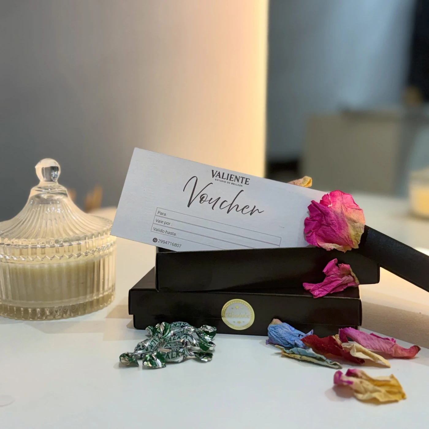 Gift card física de Valiente sobre la mesa del estudio, junto a un vaseo de cristal y pétalos de rosa